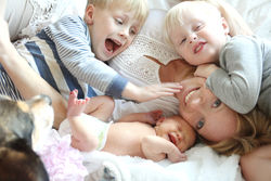 stock-photo-a-happy-young-mother-is-laying-on-the-bed-in-chaos-with-her-three-young-children-two-wild-boys-263362403